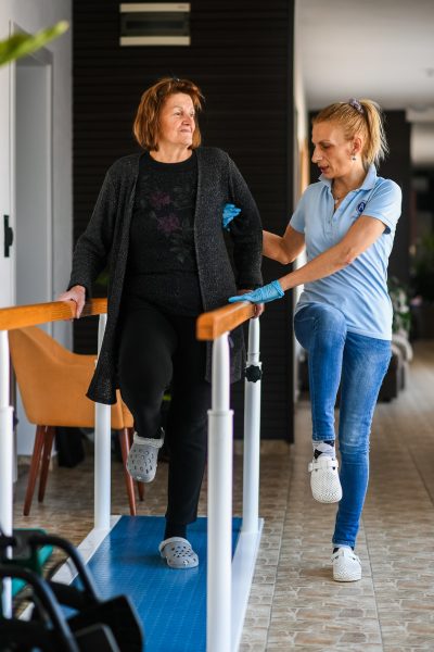 Starija žena izvodi vežbe hodanja uz podršku terapeuta radi jačanja mišića i poboljšanja ravnoteže